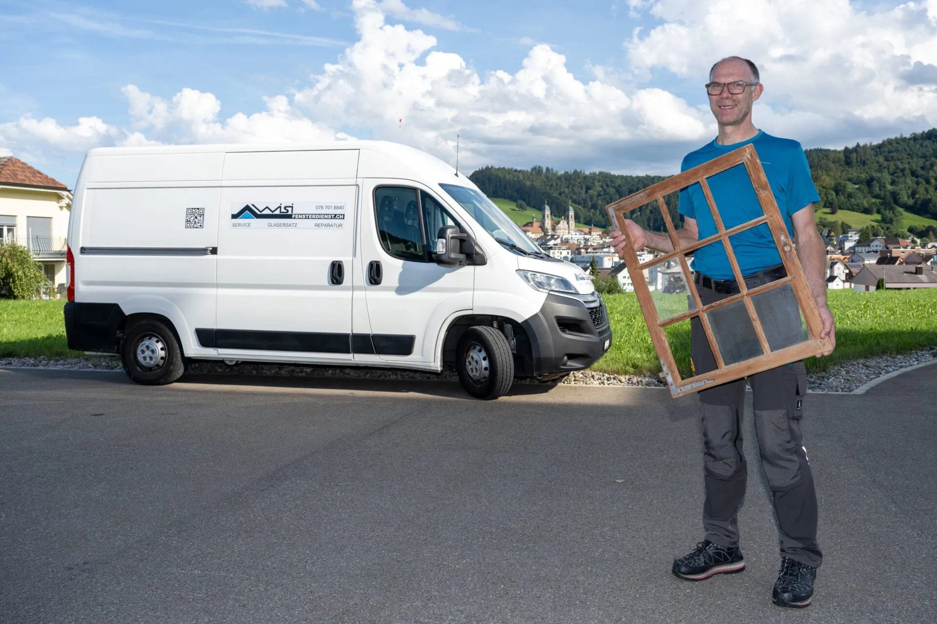 Martin Röllin steht mit einem alten Sprossenfenster vor dem Servicebus, im Hintergrund das Kloster Einsiedeln